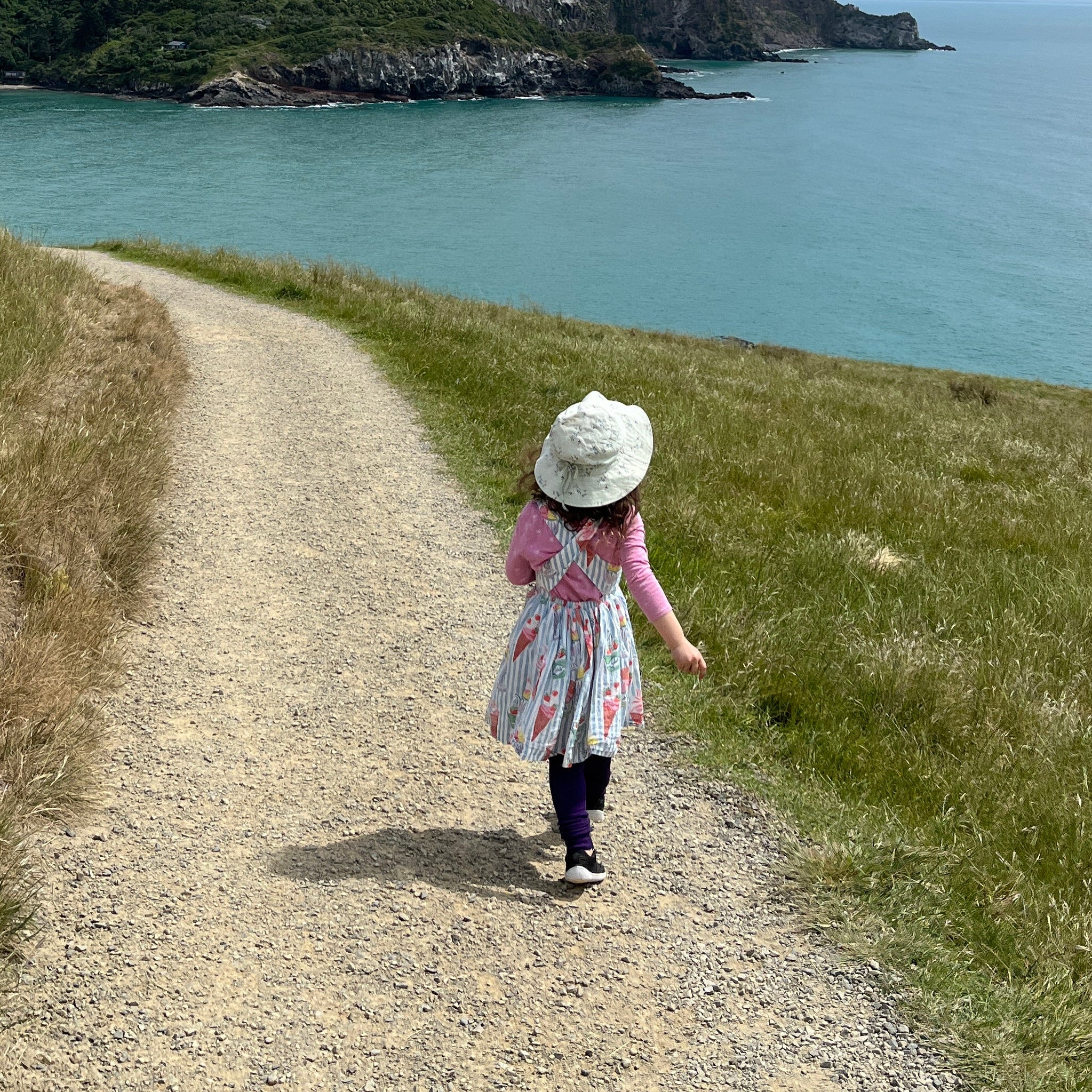 Person standing on a path near a body of water with a castle-like structure in the background.